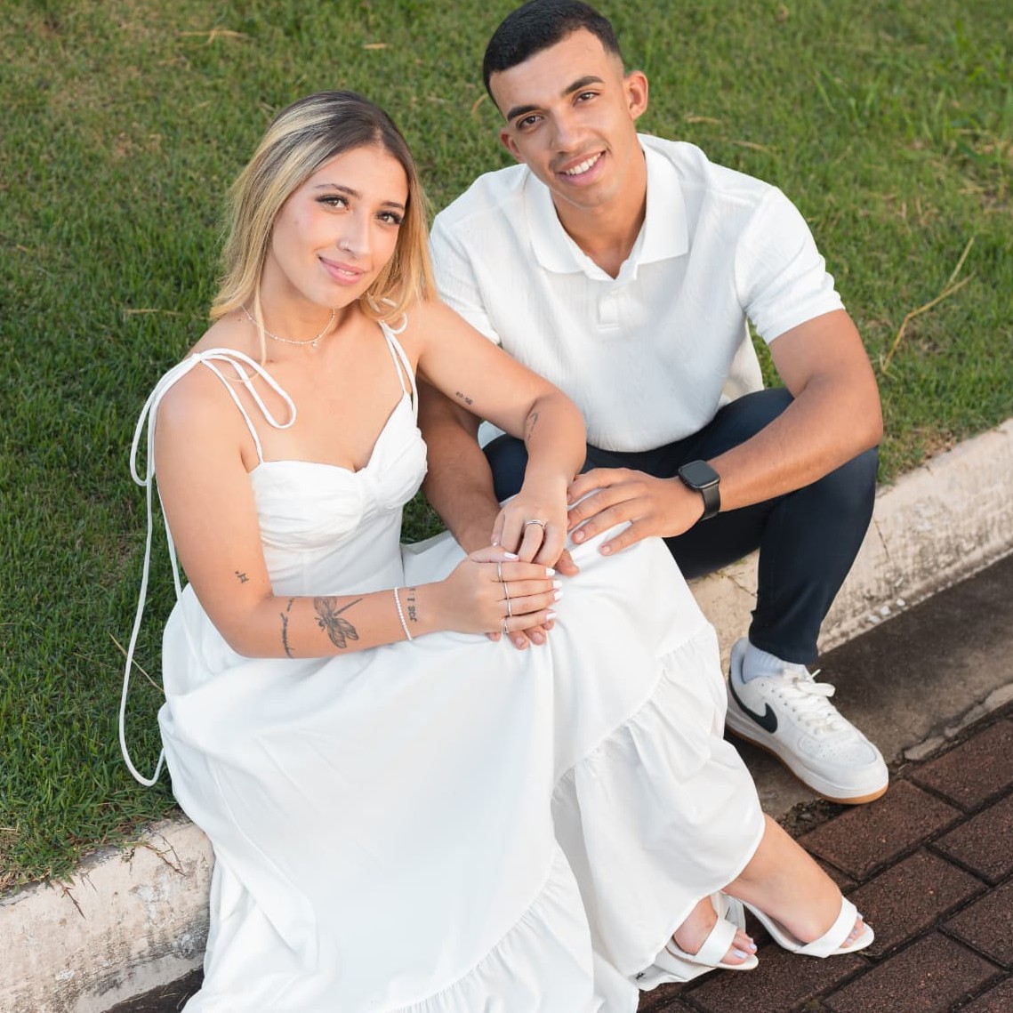 Alysson e Eduarda sentados no gramado, vistos de cima